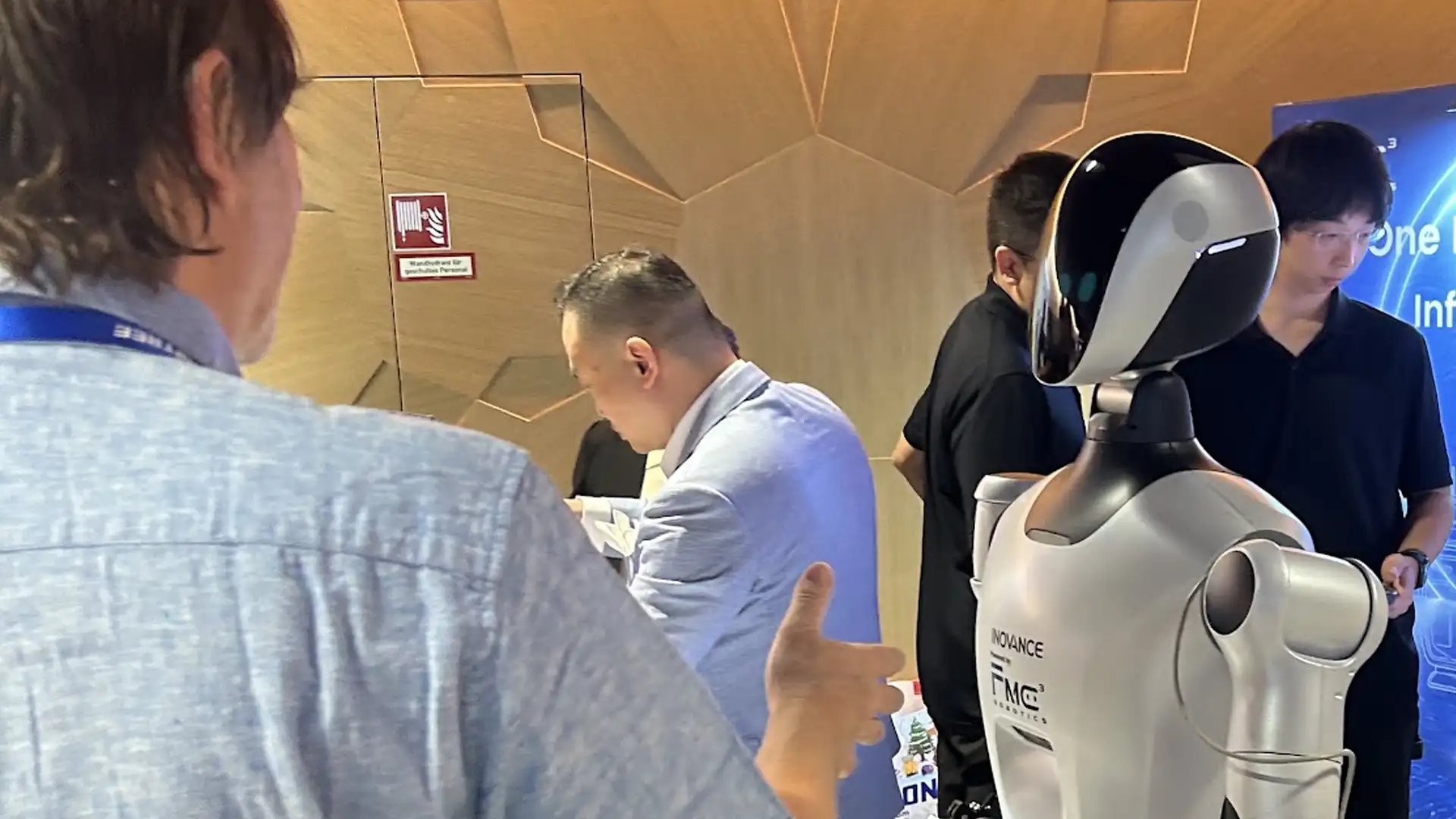 Inovance humanoid robot powered by FMC3 Robotics on the exhibition floor at the Humanoid Robots Summit in Stuttgart, attendees in conversation around it